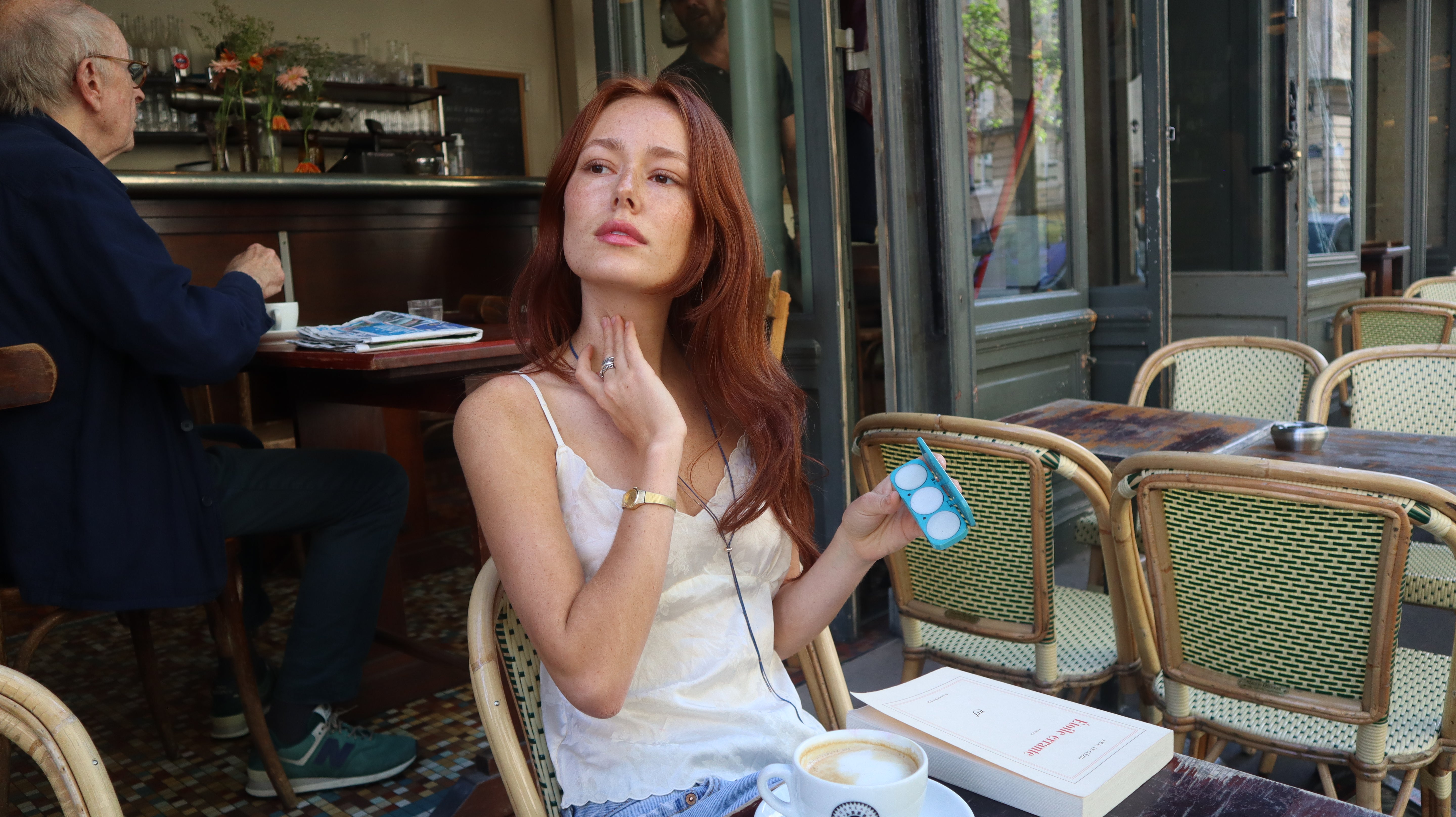 Woman sitting at a Paris cafe and applying solid perfume to her neck